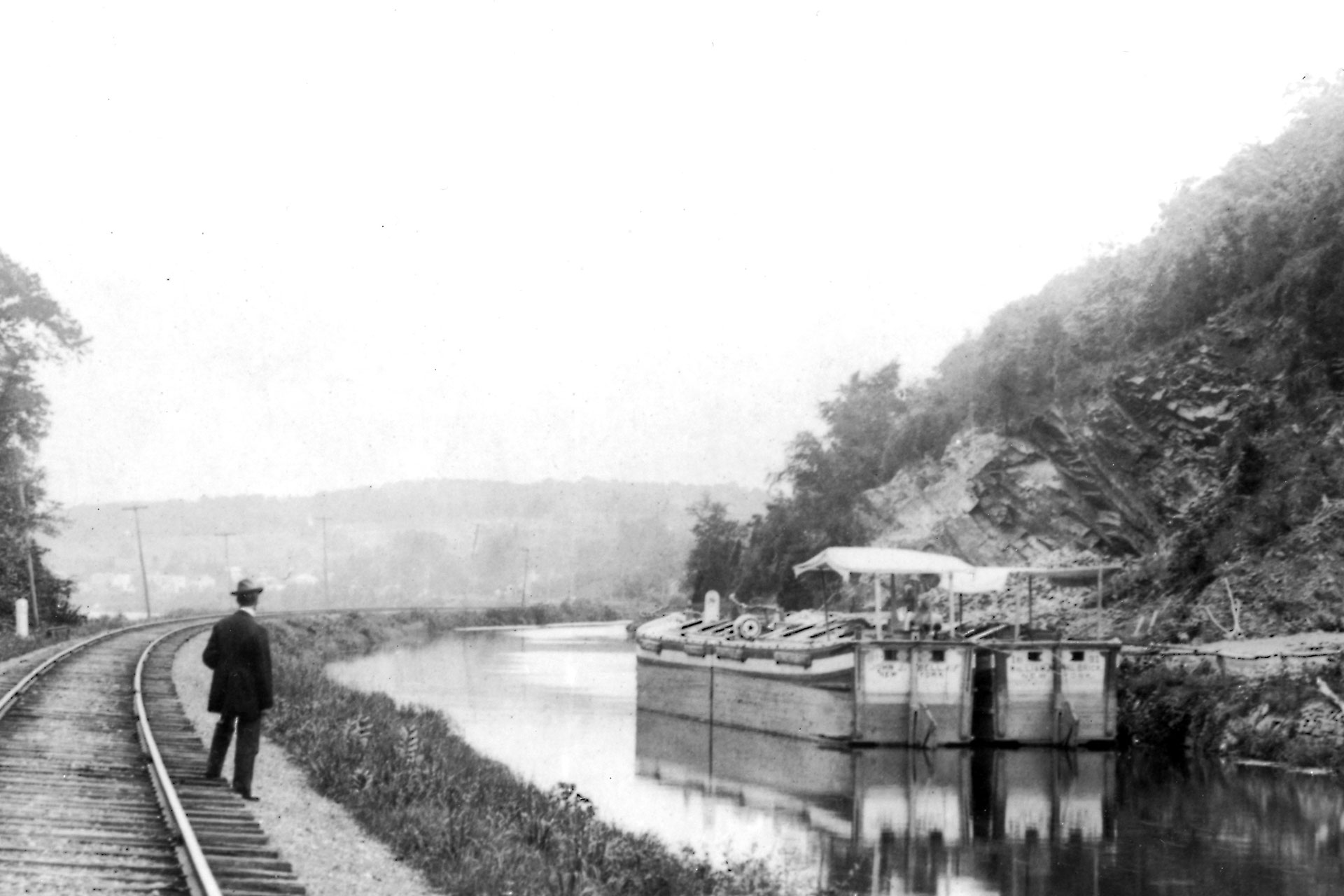 A man observes a pair of canal boats docked on the D&R Feeder. Empty, or light boats sat very high on the water. Canopies on the stern protected the captain from the hot sun.